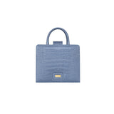 A front-facing view of the GAIA blue croc-embossed leather midi bag featuring a gold-toned GAIA logo plaque at the bottom center, two rolled top handles, and a clean, symmetrical silhouette.