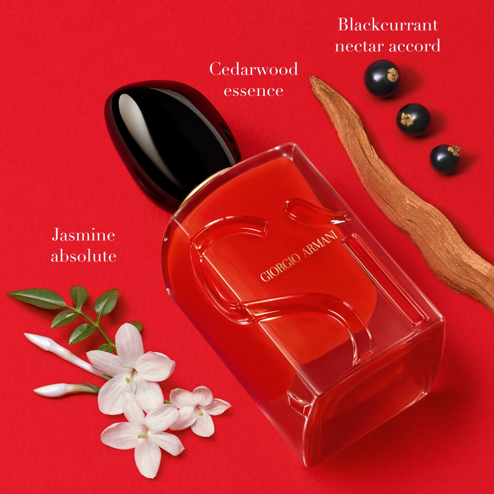 Red Giorgio Armani perfume bottle with floral and fruit elements on a red background.
