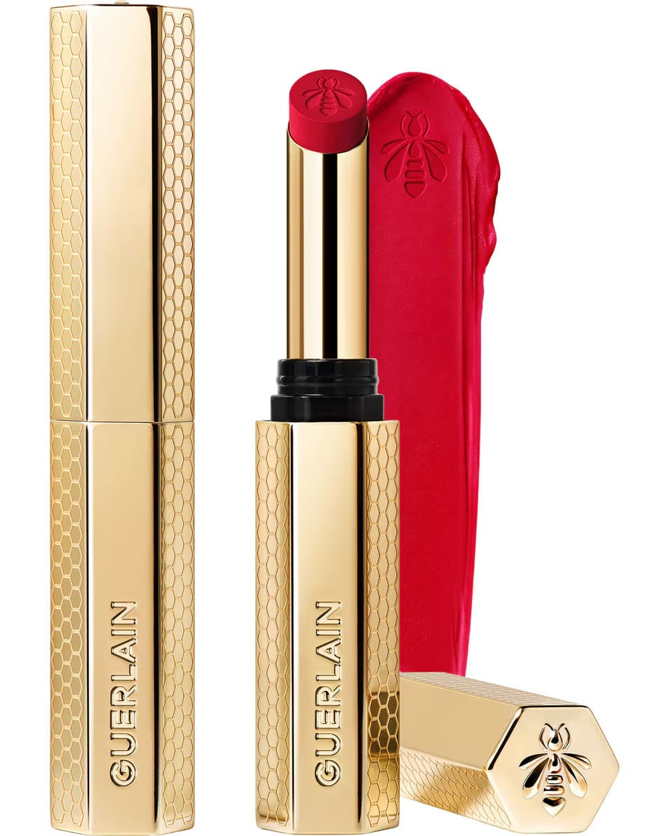 Guerlain KissKiss Honey-Infused Matte Lipstick in its signature slim golden honeycomb case, alongside an open cherry-red lipstick bullet and creamy velvety texture smudge, available at blue salon.
