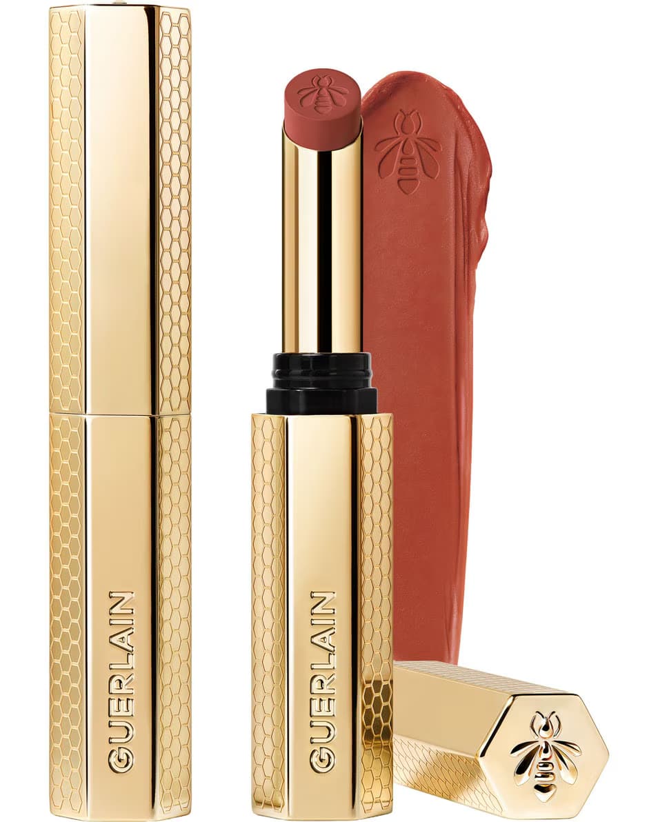 Guerlain KissKiss Honey-Infused Matte Lipstick in its signature slim golden honeycomb case, shown with an open deep burgundy-brown lipstick bullet and a velvety color smudge texture, available at blue salon.