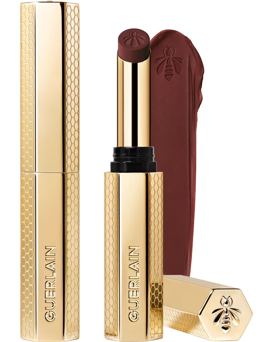 Guerlain KissKiss Honey-Infused Matte Lipstick in its signature slim golden honeycomb case, shown with an open deep burgundy-brown lipstick bullet and a velvety color smudge texture, available at blue salon.