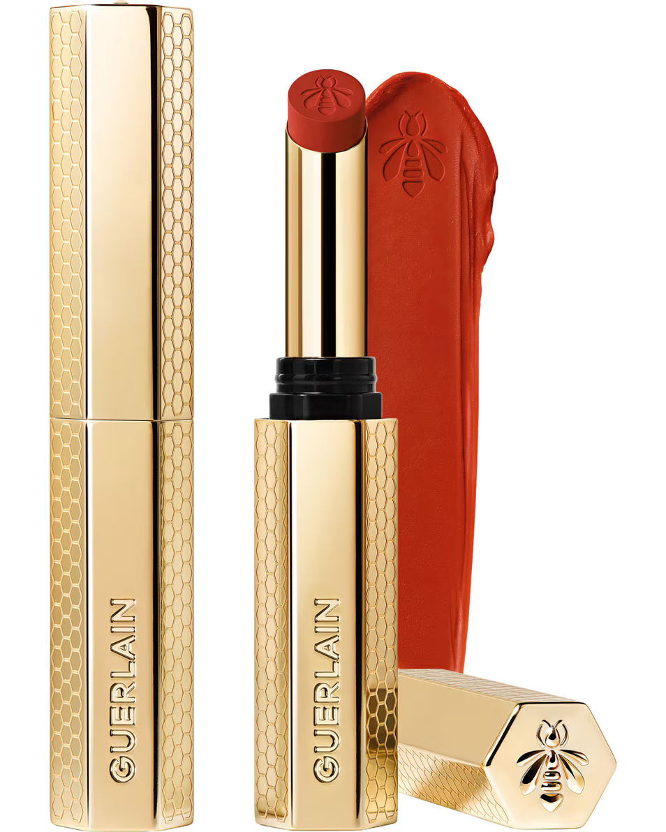 Guerlain Rouge G Honey-Infused Matte Lipstick in its signature slim golden honeycomb case, alongside an open bullet and a vibrant orange-red creamy texture smudge, from blue salon.