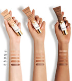 Three hands of different skin tones holding Guerlain Terracotta Joli Teint tubes next to arm swatches labeled from shades 10 to 50, available at blue salon.