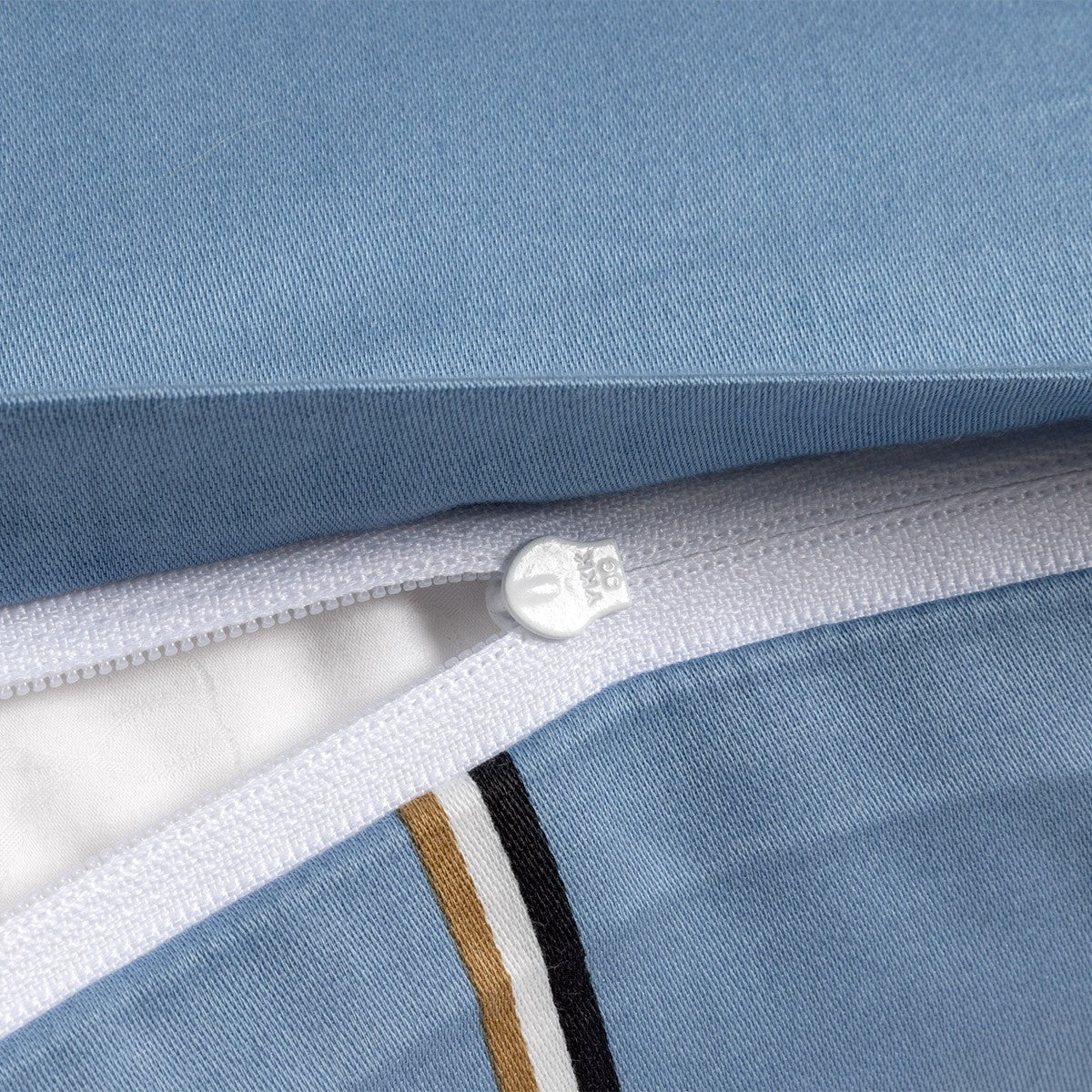 Light blue fabric duvet cover with a white zipper and a decorative stripe of gold-toned, white, and black bands.