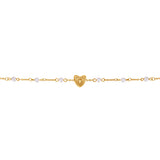 A detailed linear macro shot focusing on the center of the Escada Mina bracelet, highlighting the textured lines of the golden heart charm nestled between symmetric stations of white pearlescent beads.