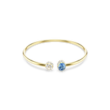 A high-resolution direct frontal studio shot of the Swarovski Chroma open bangle laid out on a white surface, displaying its sleek gold-plated band and contrasting blue oval and white round crystal terminals.