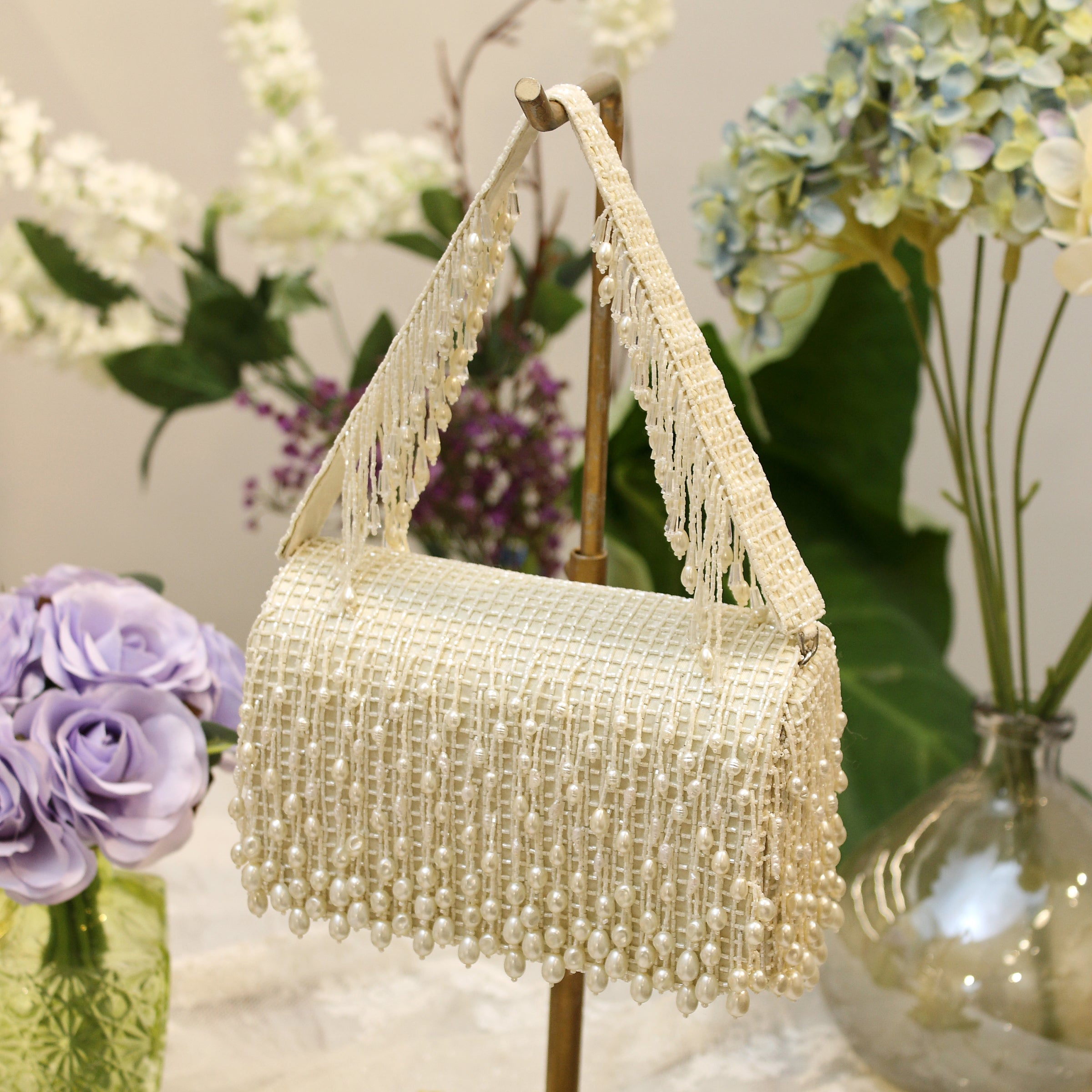 Pristine ivory clutch bag with a textured body and strap, entirely covered in dangling pearl-like beads forming a fringe.