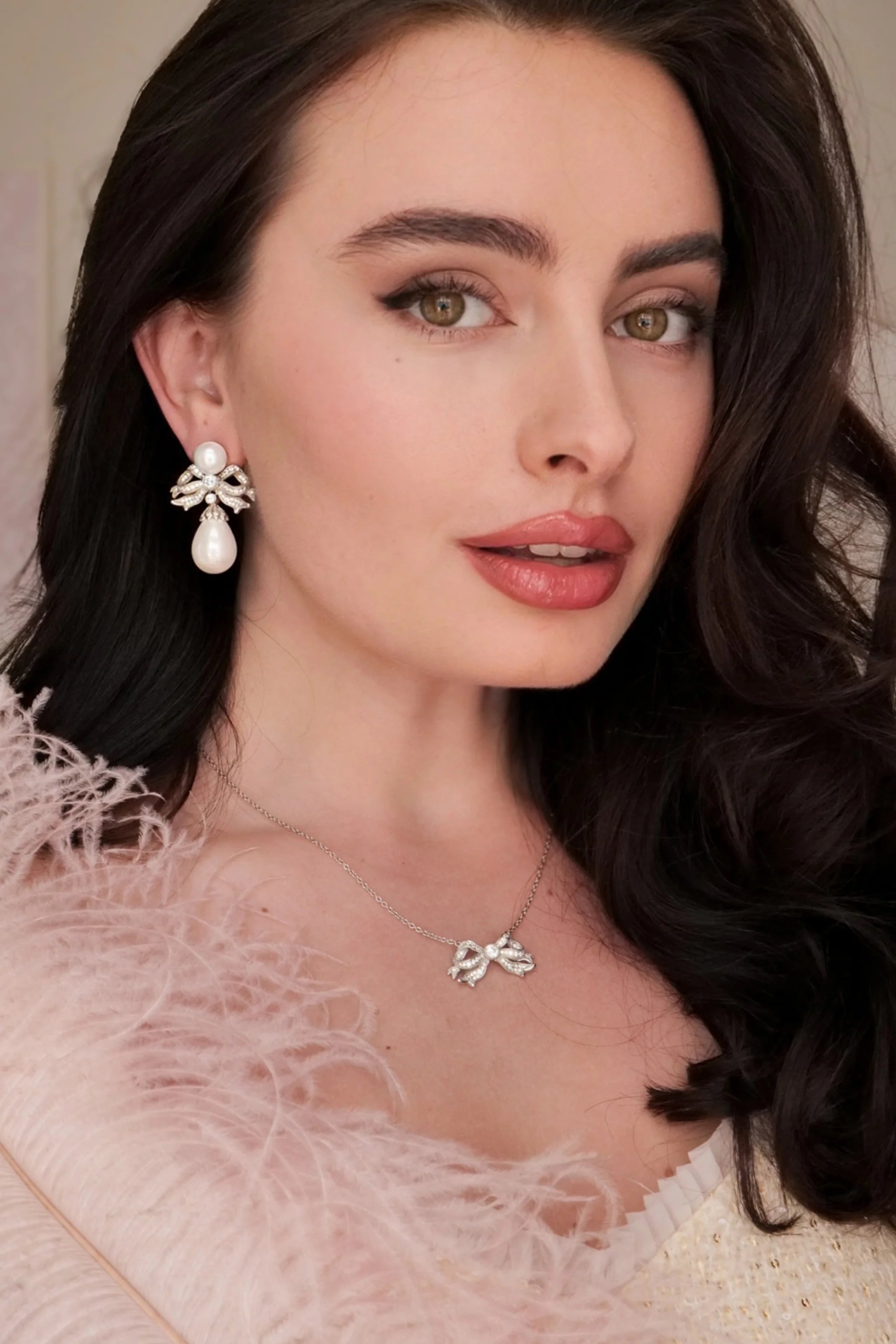 Silver-toned necklace with a thin chain and a bow-shaped pendant encrusted with clear stones, featuring a larger stone at its