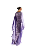 Back View of woman modeling a Velvety brand lavender two-piece set. The inner gown is covered in silver sequin wave patterns, while the outer chiffon layer features dramatic cascading ruffles and a fluid, tiered hemline.