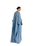 A woman modeling a Velvety brand sky-blue two-piece set. The inner dress is a column-style gown with a square neckline and extensive tonal beadwork. The outer layer is a matching floor-length cape with a crinkled texture and wide, flowing sleeves.