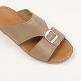 Taupe leather slip-on sandal with a wide strap, silver-toned buckle, and tan leather insole with white stitching.