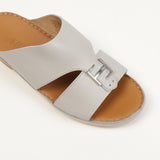 Light grey leather slide sandal with a wide strap, inner cut-out, silver-toned buckle, and tan footbed with visible stitching