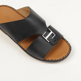 Black leather slip-on sandal with a tan insole and a wide strap featuring a silver-toned T-shaped buckle.