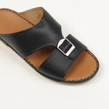 Black leather slide sandal with a wide, cutout strap, silver-toned buckle, and tan leather insole with visible stitching.
