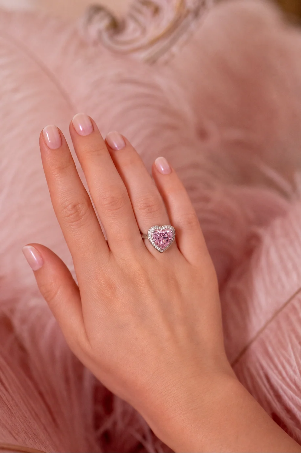 Silver-toned ring with a large light pink heart-shaped gem surrounded by a halo of small clear stones.