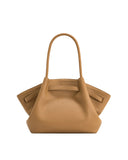 Tan pebbled leather medium tote bag with a single curved top handle. The sides fold inward, secured by horizontal straps.