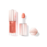 Clear rectangular lip gloss tube with peachy-pink liquid, "LANCOME" text, and rose gold-toned faceted cap. White applicator w