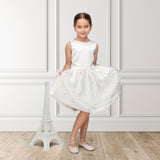 A luxury ivory occasion dress shown alongside a Jules & Juliette Paris 3-piece baby gift set in grey Toile de Jouy.