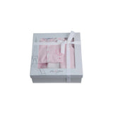 A luxury 3-piece baby girl gift set by Jules & Juliette Paris in light pink. Images show a footed romper with hot air balloon embroidery, a matching pink beanie with picot trim, and a reversible white and pink patterned blanket. The set is also shown packaged in a signature grey window gift box with a white ribbon.