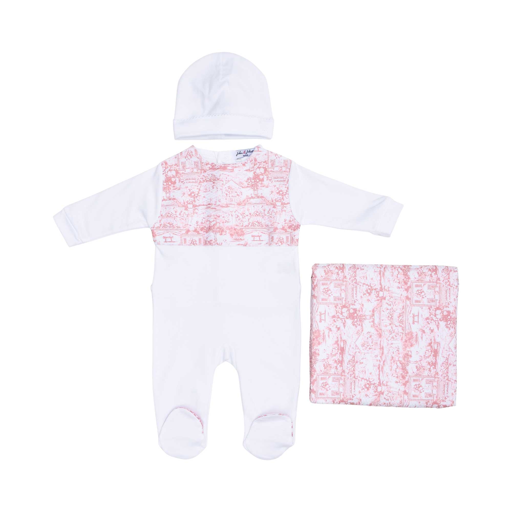 Front view of the Jules & Juliette Paris baby set featuring a white sleepsuit with a pink Toile de Jouy chest panel, a white hat, and a folded blanket.