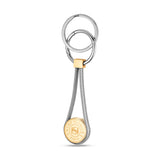 Silver-toned keyring with two rings, a gold-toned square, and two silver-toned coiled strands holding a gold-toned coin with