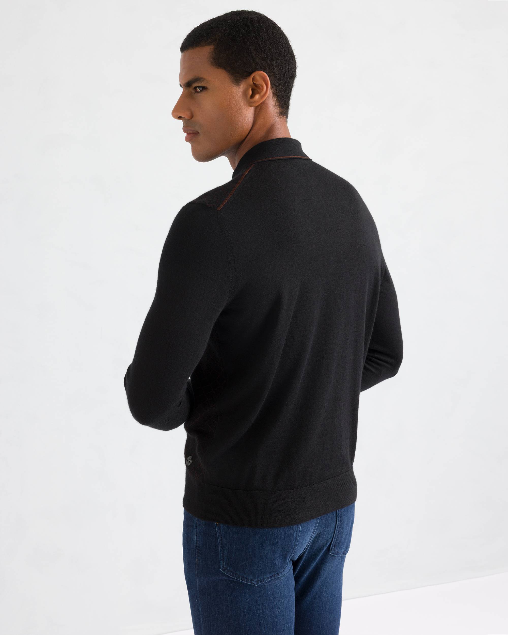 Black fine-knit sweater with a brown-trimmed collar, shoulder stitch detail, ribbed cuffs and hem, and a silver-toned emblem.