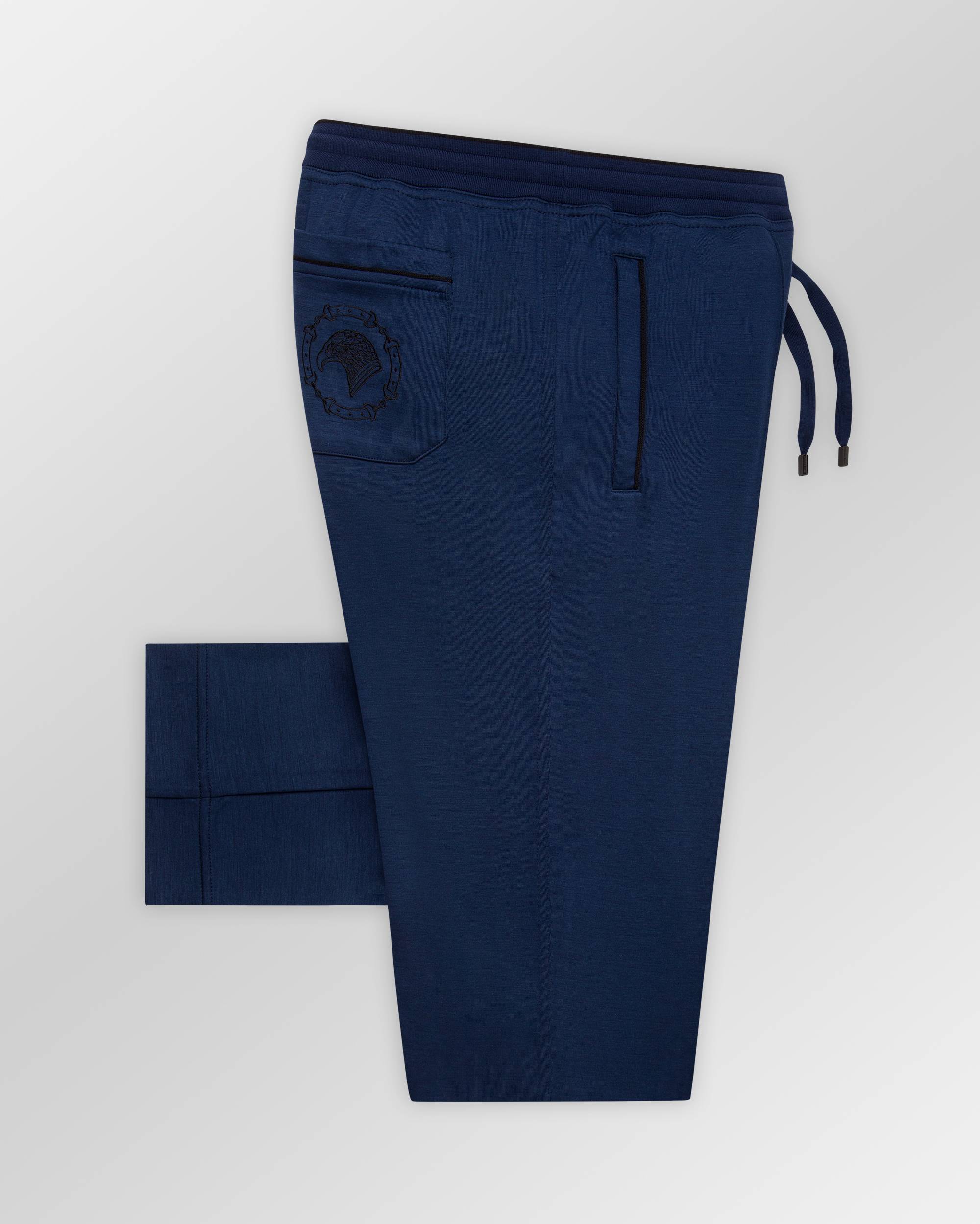 Blue sweatpants with a darker elastic waistband, drawstring, black-trimmed pockets, black embroidered emblem, and cuffed ankl