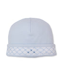 Light blue knit baby hat with a white smocked brim featuring light blue diamond pattern and three small blue embroidered dots