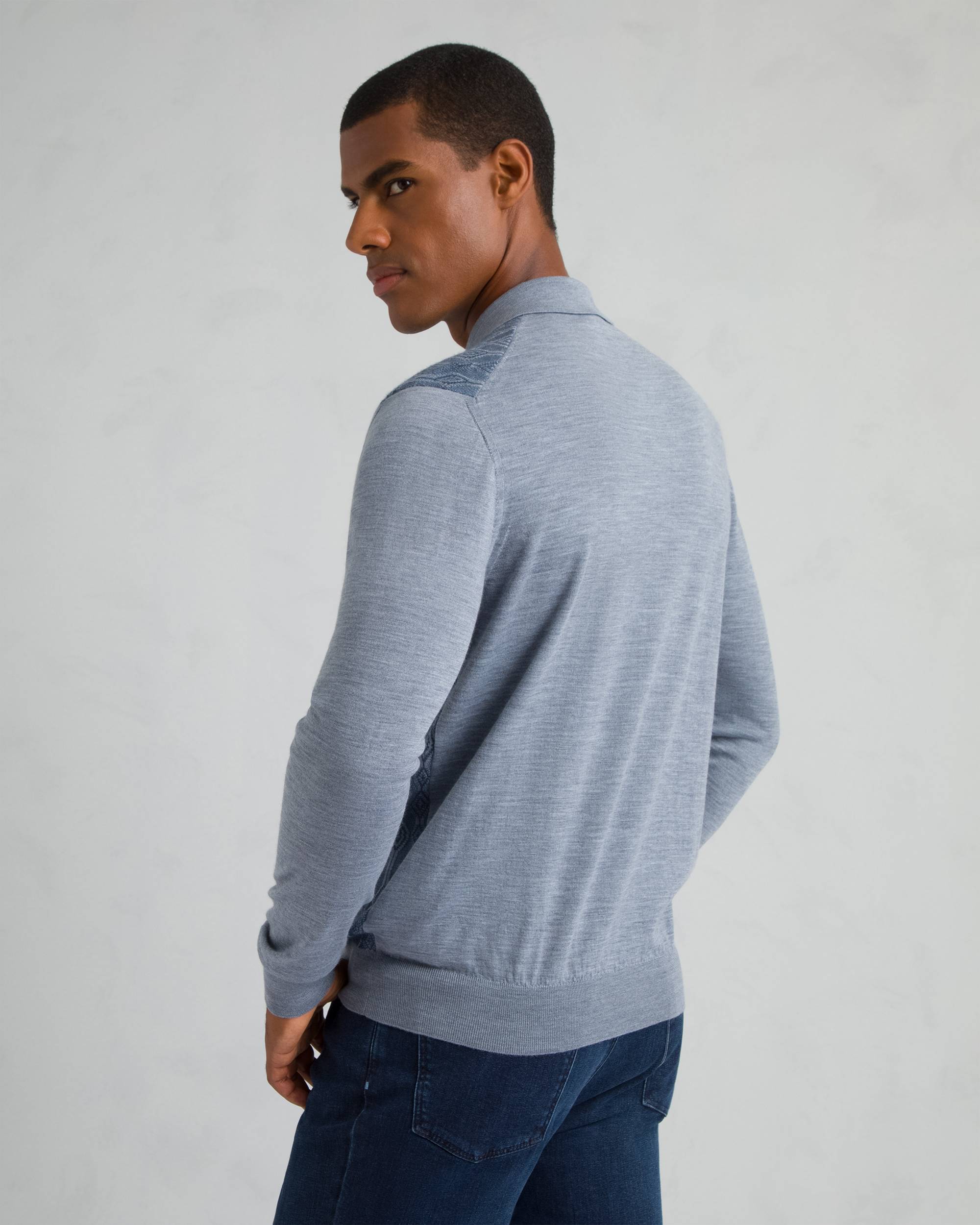 Light blue long-sleeve polo sweater with ribbed collar, cuffs, and hem. Features darker blue patterned panels on shoulders an