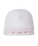 White newborn girl's cap with a folded brim featuring pink smocking and small embroidered pink roses.