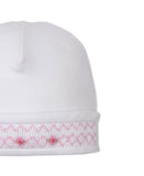 White baby beanie with a folded brim featuring pink smocking and small embroidered pink roses with green leaves.