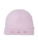 Light pink baby beanie with a folded brim featuring white smocking and small embroidered pink roses with green leaves.