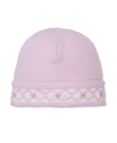 Pink baby beanie with a white smocked brim featuring pink diamond patterns and small pink bows.