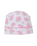 White baby beanie with scattered pink floral clusters and green leaves, featuring a ruffled pink trim above the folded white