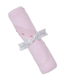 Rolled pink blanket with a diagonal white smocked band featuring small pink embroidered roses and leaves. Tied with a gray 'k