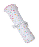 White blanket rolled up, covered in small pink, blue, yellow, and orange hearts. One end has a pink-edged ruffle. Tied with a