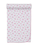 White baby blanket with a scattered pink tulip floral pattern and pink scalloped edges, rolled at the top.