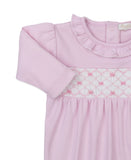 Pink long-sleeved sleepsuit with a ruffled neckline and a white smocked panel featuring pink embroidered bows.