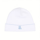 White baby beanie with a light blue scalloped trim and a small embroidered light blue teddy bear on the front.