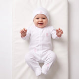 White sleepsuit with pink trim, snap closure, and pink teddy bear embroidery on chest, thigh, and shin. Matching white beanie
