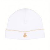 White baby beanie with a light tan scalloped trim and a small embroidered teddy bear design.