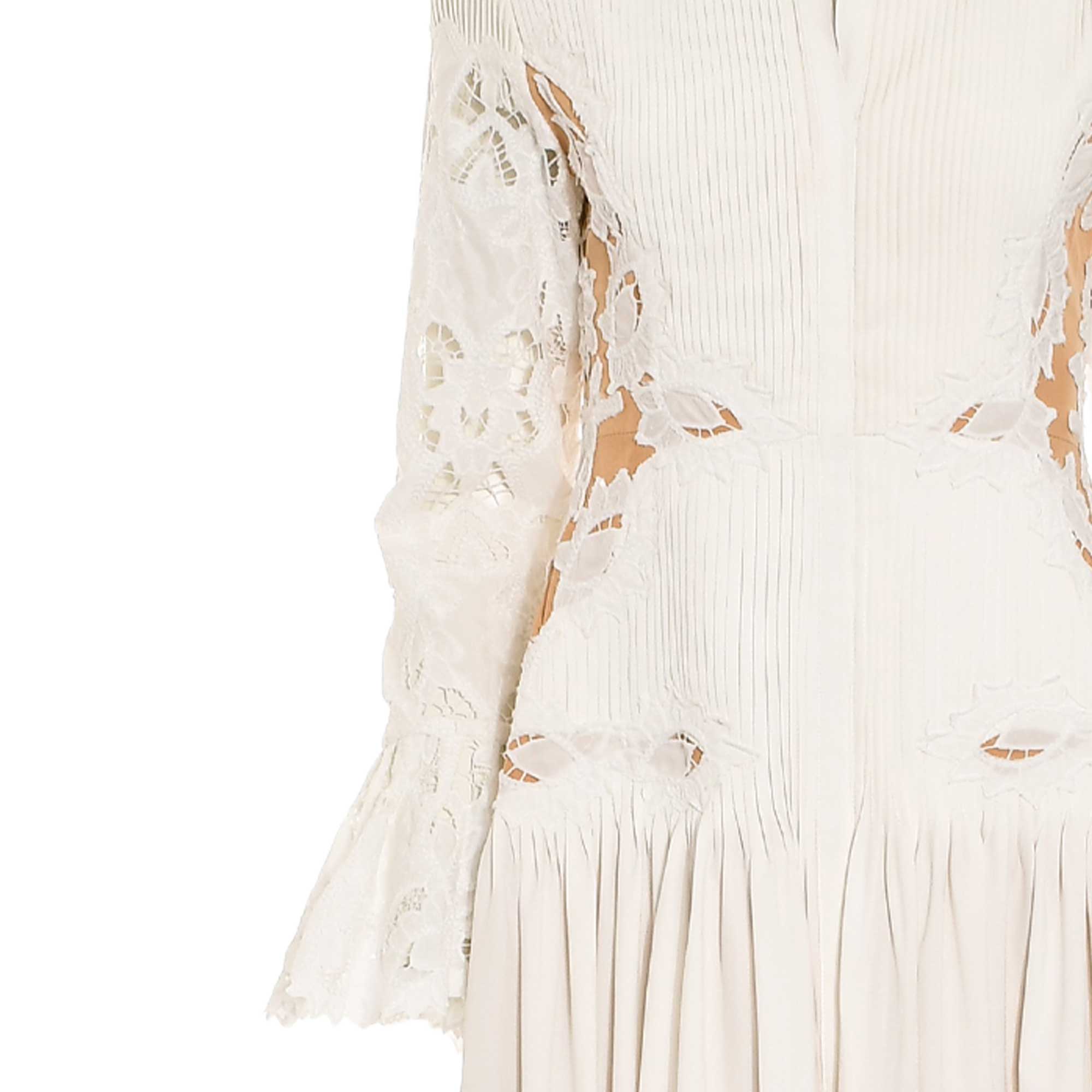 White pleated dress with long lace sleeves featuring cutouts and ruffled cuffs. Bodice has vertical pleats and leaf-patterned