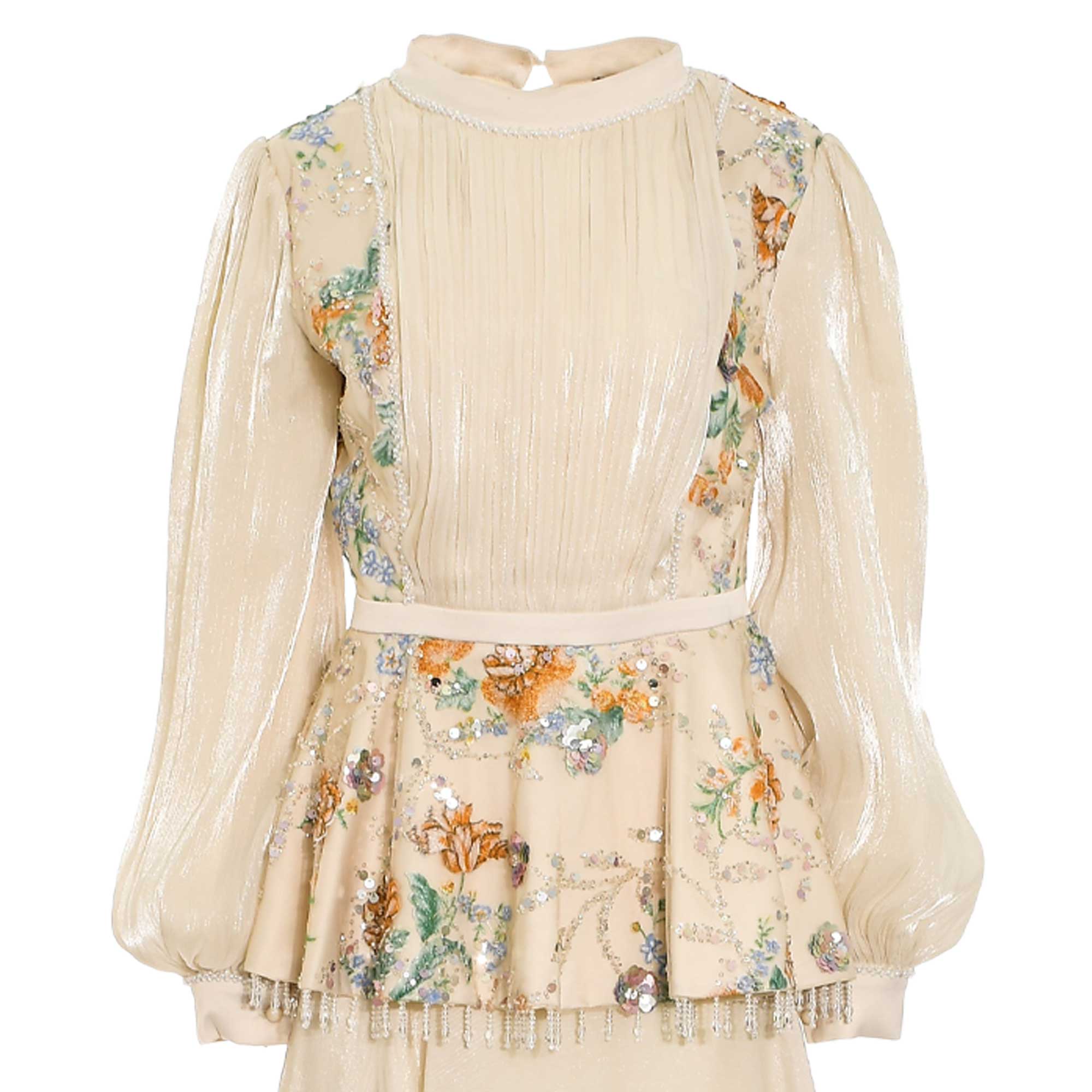 Beige top and skirt. Shimmery pleated top with beaded high neck, long puffed sleeves. Floral embroidered panels and peplum wi
