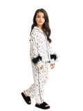 Full-length front studio shot of a young girl walking while modeling the Katee's Kids white silk pajama set, highlighting the black contrast piping, front buttons, and plush black feather cuffs.