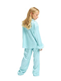 A three-quarter back view of a young blonde girl modeling a turquoise silk pajama set from Katee's Kids, showcasing the relaxed drape and a tonal feather-trimmed cuff against a white studio background.