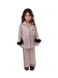 Full-length front studio shot of a young girl modeling the Katee's Kids blush pink silk pajama set, detailed with black piping, front buttons, and black feather-trim cuffs.