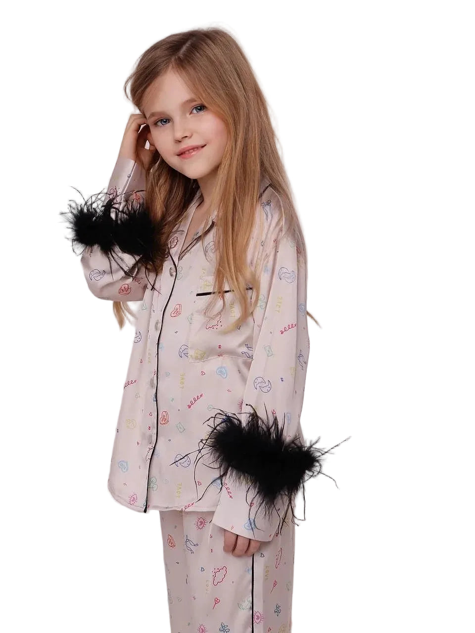 A side view of a young blonde girl smiling in a light pink silk pajama set with a colorful doodle print, showcasing the prominent black feather cuffs on the sleeves against a studio background.