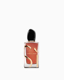Clear rectangular perfume bottle with reddish-orange liquid, a black oval cap, and gold-toned abstract shapes. "GIORGIO ARMAN