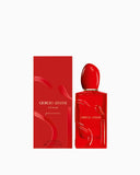 Red rectangular perfume bottle with red oval cap, gold-toned neck, embossed text, and curved red designs. Matching red box.