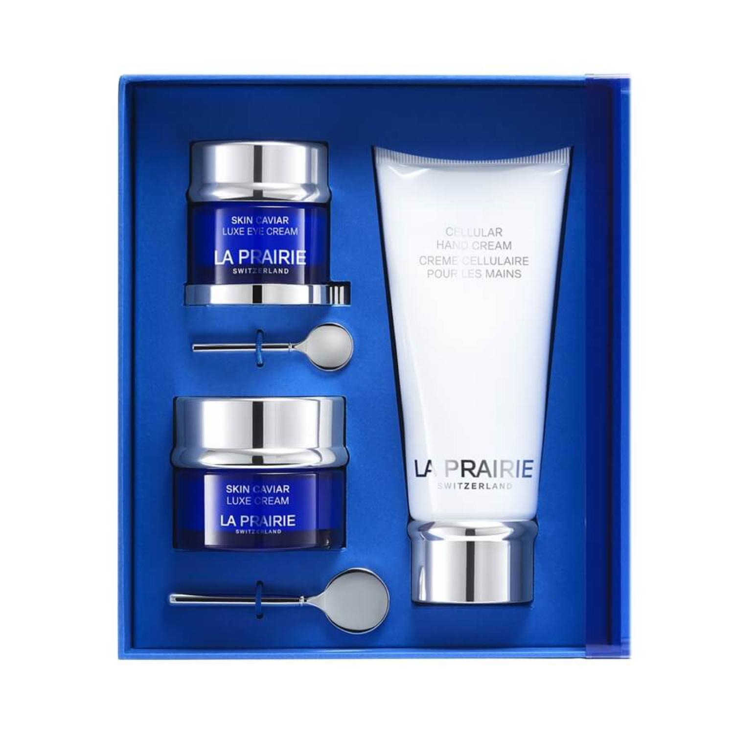A luxury La Prairie Switzerland skincare gift set in a cobalt blue presentation box. The set features Skin Caviar Luxe Eye Cream (20ml) and Skin Caviar Luxe Cream (50ml) in signature blue glass jars, alongside a large white tube of Cellular Hand Cream (100ml). Two silver application spatulas are included for precise use.